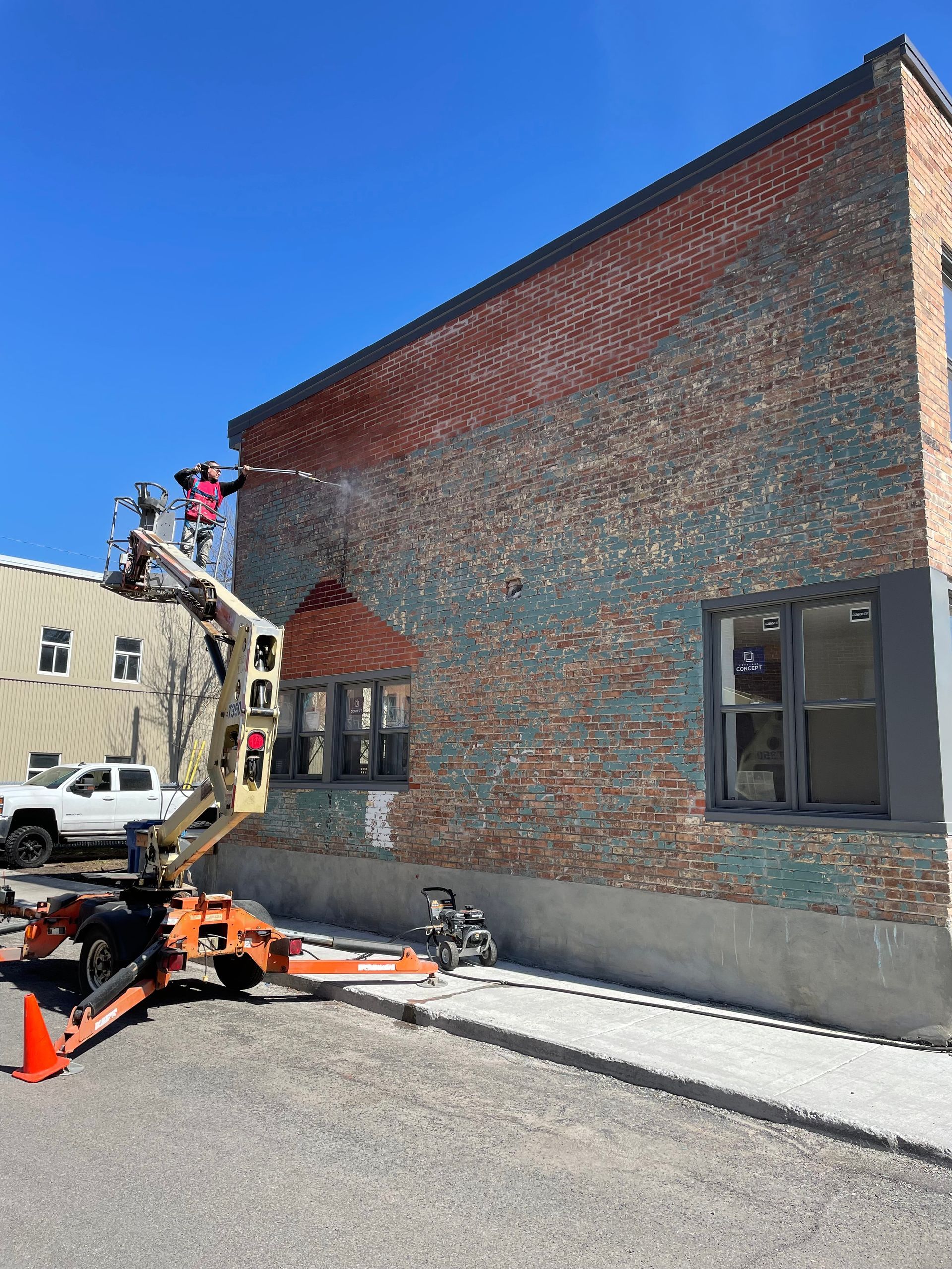 Un ouvrier du bâtiment, sur une nacelle, peint la façade d'un immeuble en briques ; briques bleues et rouges.
