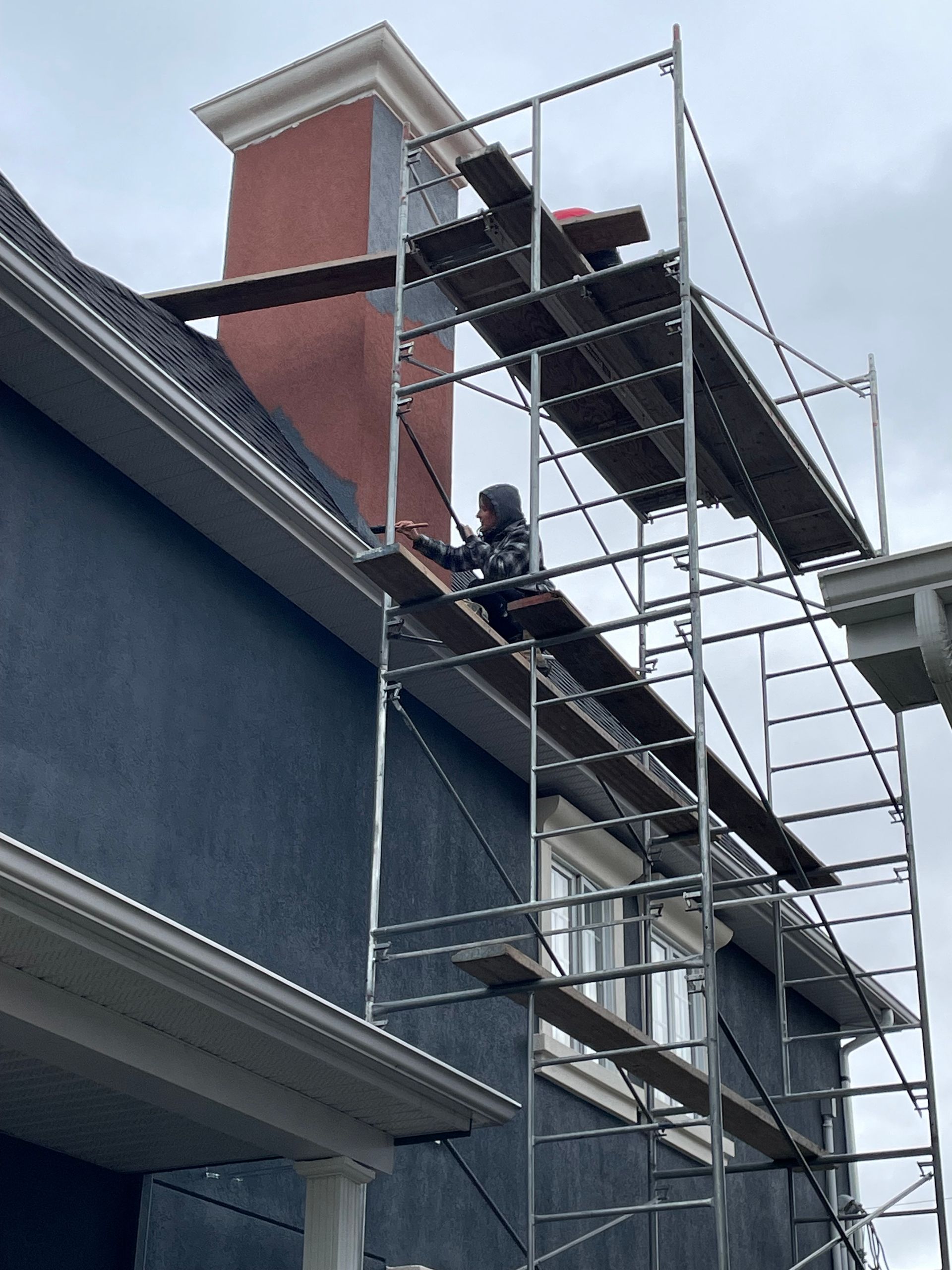 Une personne travaille sur un échafaudage près d'une cheminée sur une maison bleu foncé.