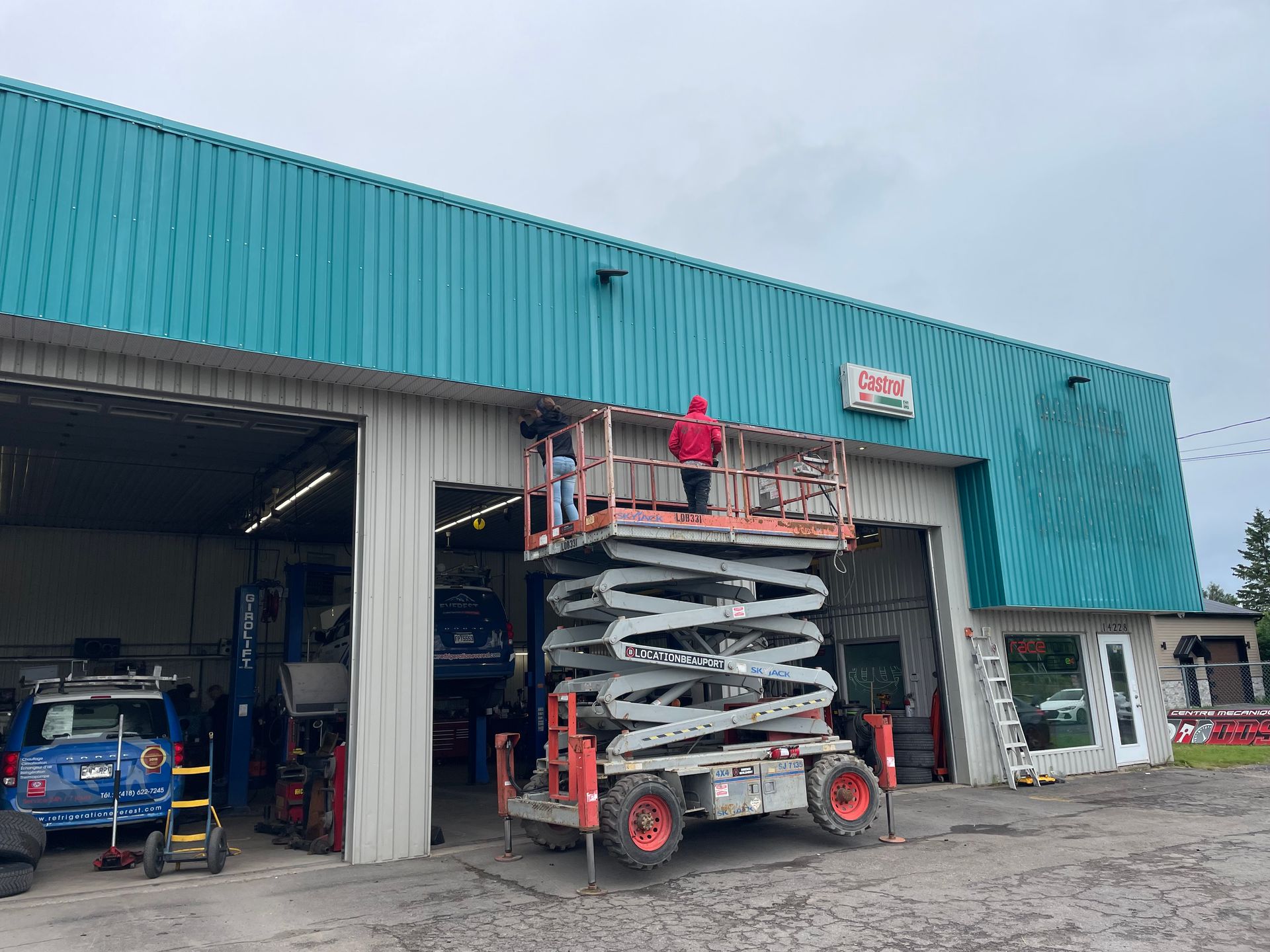 Deux personnes travaillent sur une nacelle, au-dessus d'un garage, sur l'enseigne d'un immeuble