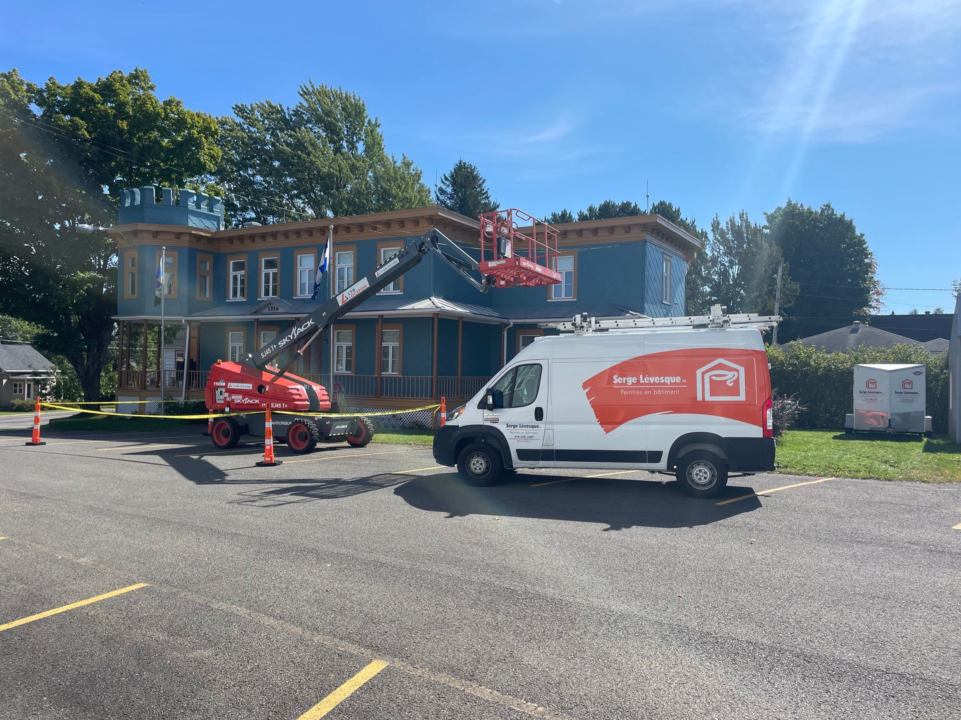 Maison bleue en rénovation ; ascenseur rouge et camionnette blanche sur place.