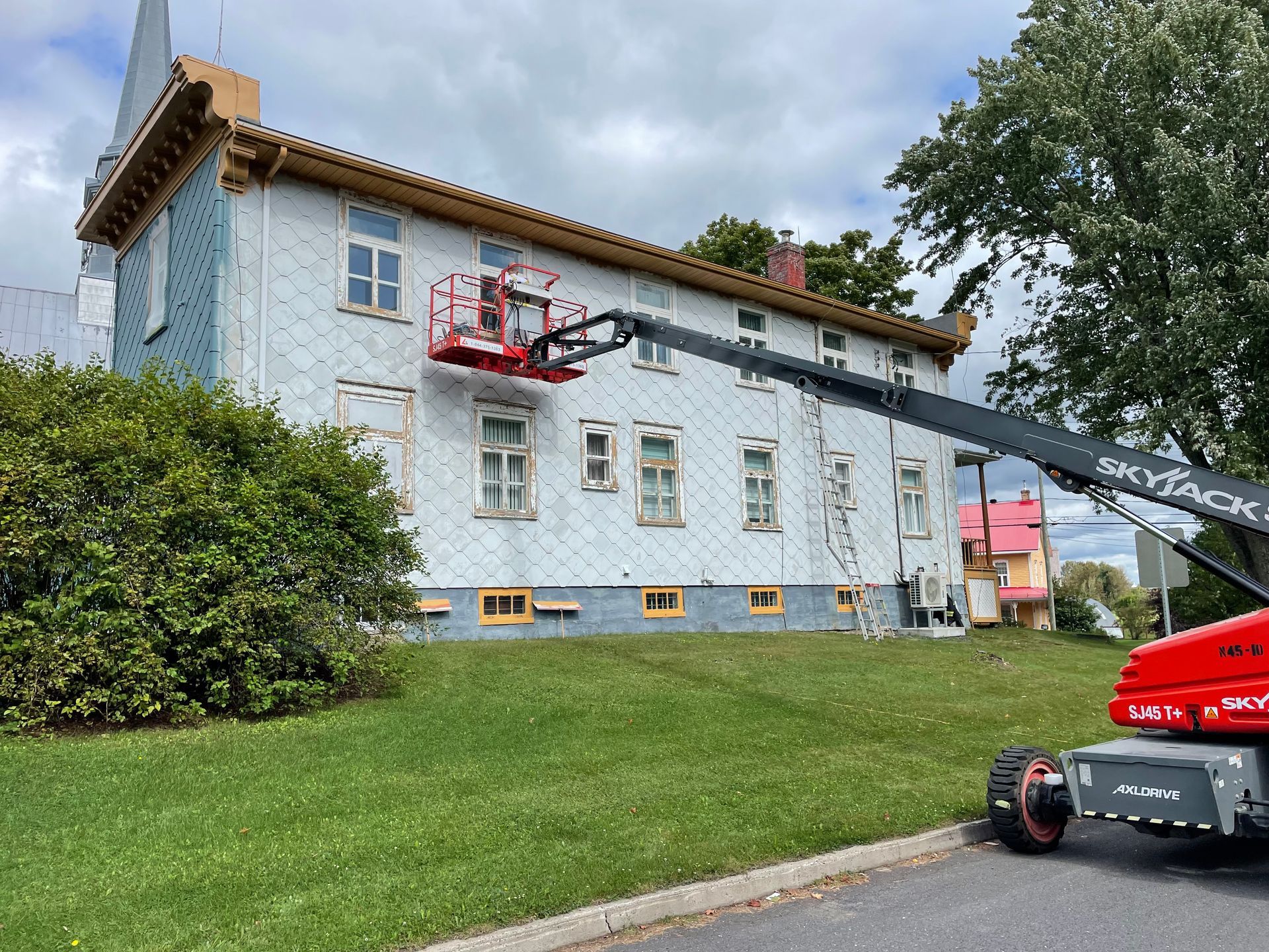 Une grue est utilisée pour peindre le côté d'un bâtiment.