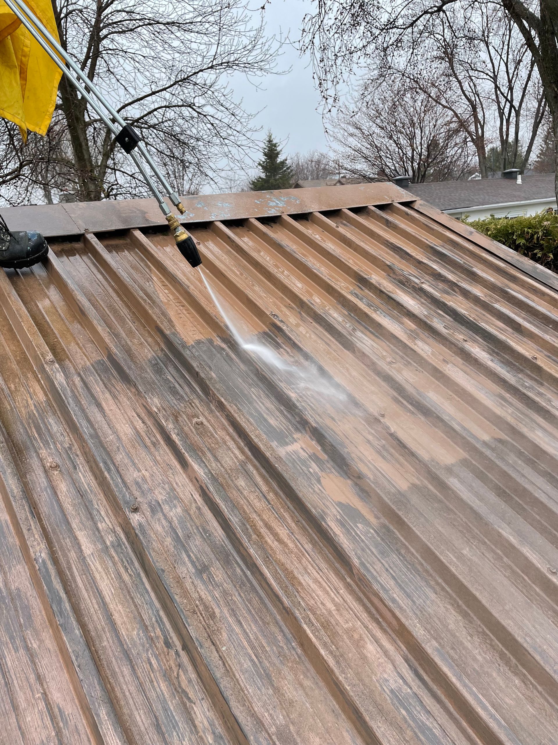 Une personne nettoie une toiture métallique avec un nettoyeur haute pression.