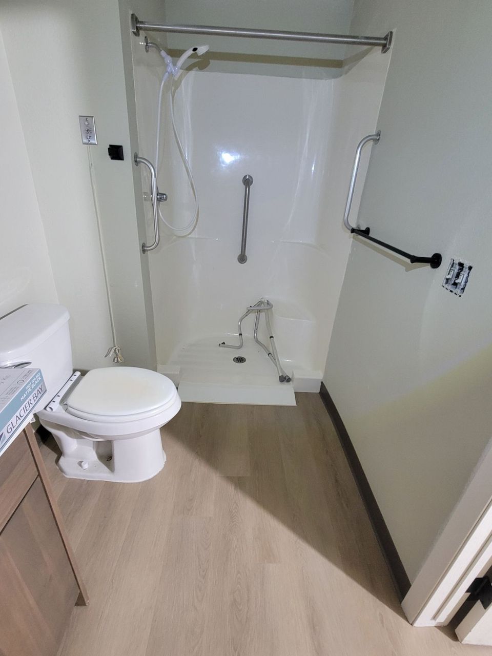 A bathroom with a toilet , shower and handrails.