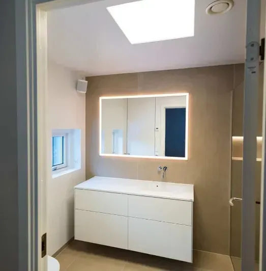 Moderne hvidt badeværelse med stort spejl, håndvask og ovenlysvindue. Beige vægfliser.
