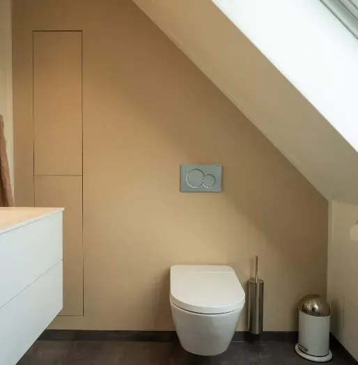 Et moderne badeværelse med toilet, håndvask og en skrå væg. Væggene er beige.