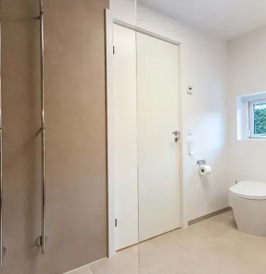 Moderne badeværelse med hvide vægge, toilet og en lukket hvid dør.