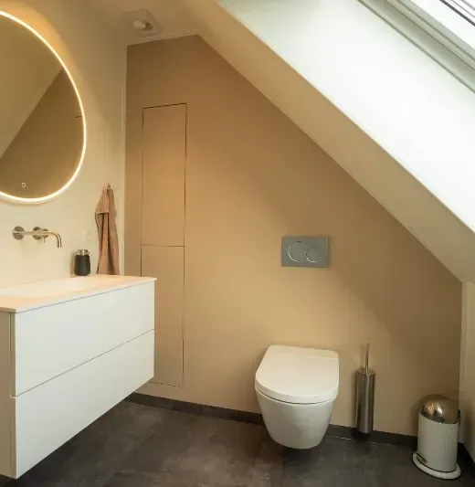 Moderne badeværelse med et hvidt svævende håndvask, et vægmonteret toilet og et skrånende loft med ovenlysvindue.