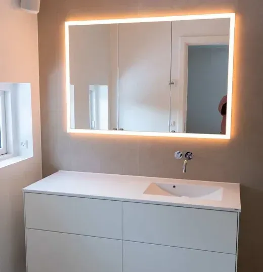 Moderne hvidt badeværelsesmøbel med oplyst spejl over en vask.