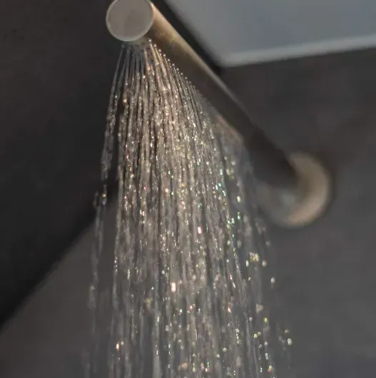 Brusehoved sprøjter vand; sølvarmatur mod en mørkegrå baggrund.