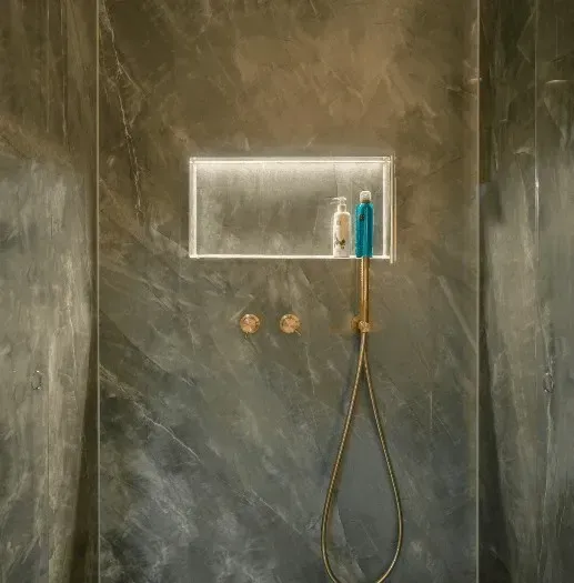 Bruser med indbygget hylde til shampoo og body wash. Messingarmaturer mod grå marmor.