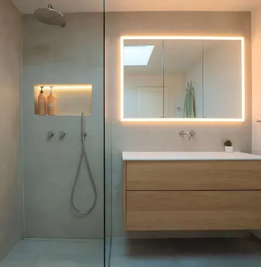 Moderne badeværelse med træhåndvask, oplyst spejl, bruseniche og grå vægge.