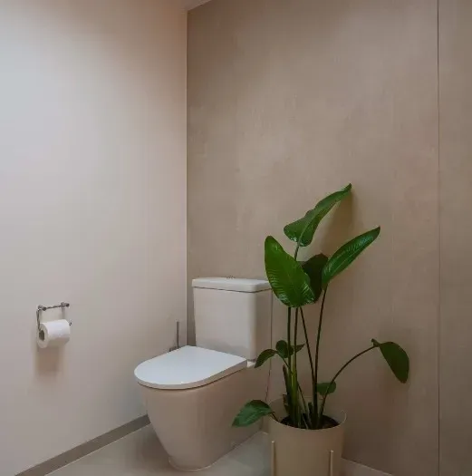 Toilet i et neutralt badeværelse med en potteplante.