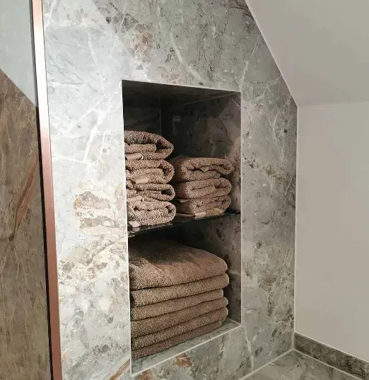 En badeværelsesniche med foldede håndklæder, indbygget i en grå marmorvæg.