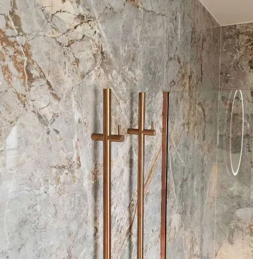 To håndklædestativer i kobber og en træliste monteret på en marmorflisevæg.