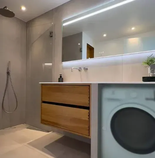 Moderne badeværelse med bruser, håndvask og vaskemaskine. Lysegrå vægge, træskab.