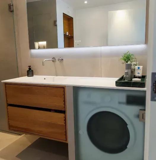 Badeværelse med træhåndvask, marmorbordplade, spejl og vaskemaskine.