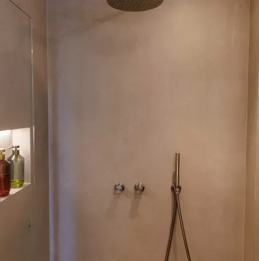 Bruser med beige vægge, et regnbruserhoved og en håndbruserstang.