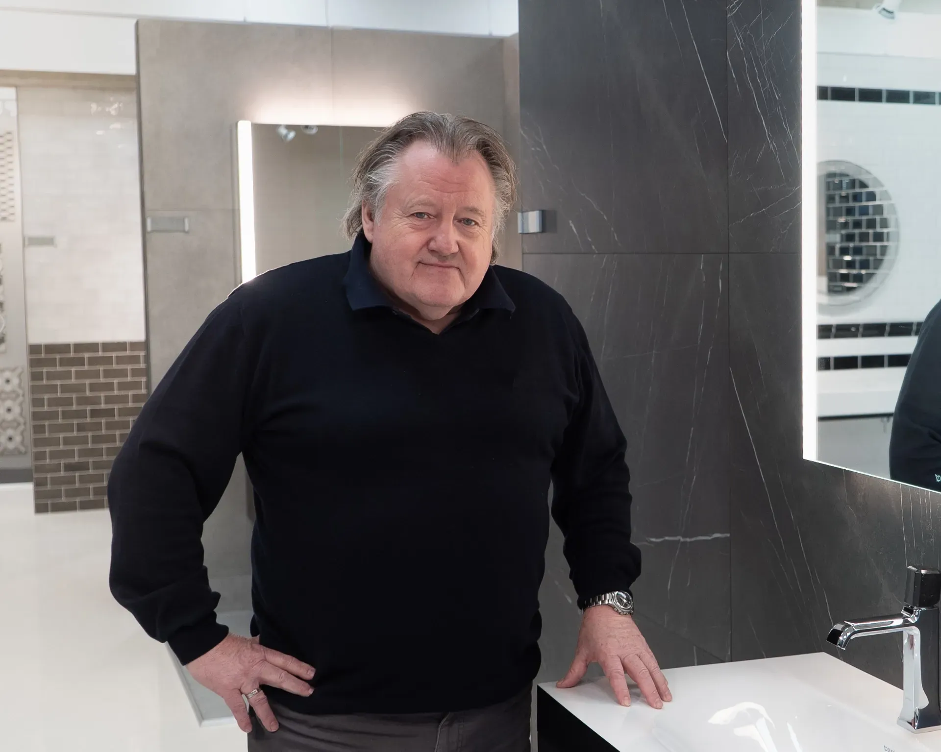 Mand i sort skjorte står ved badeværelsesvasken. Indretningsshowroom.