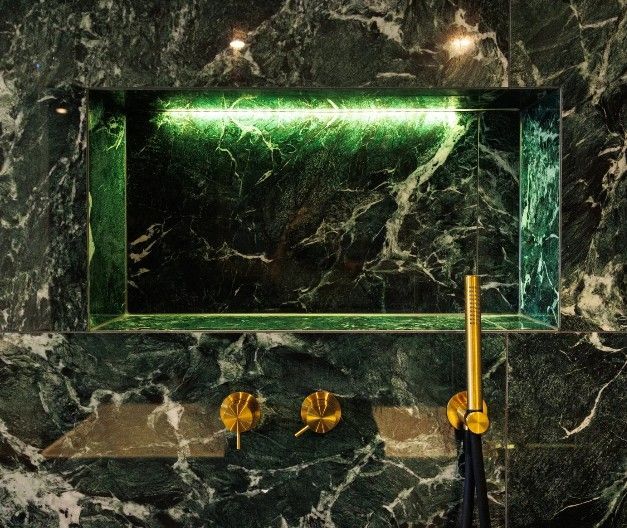 Grøn marmorbrusniche med guldarmaturer og grøn LED-belysning.