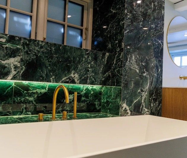 Grønt marmorbadeværelse med guldarmaturer og et ovalt spejl.