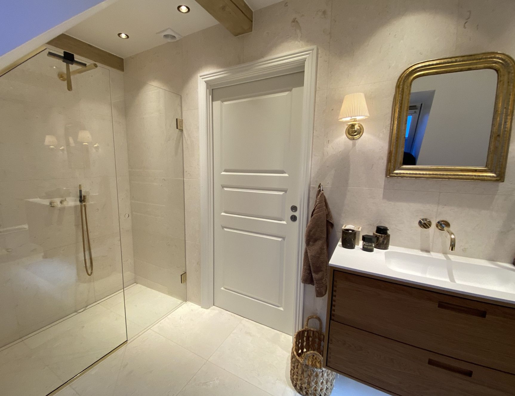 Badeværelsesindretning med bruser, håndvask, guldspejl og træbordplade.