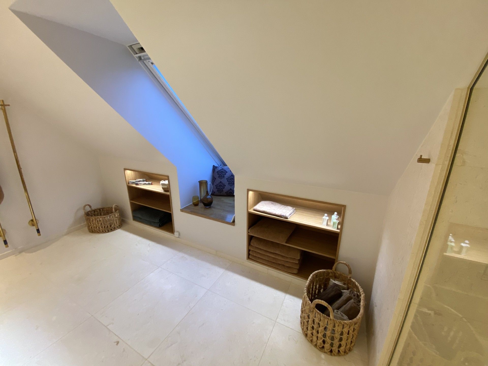 Loftsværelse med skrånende loft, indbyggede hylder og kurve, oplyst af blødt lys.