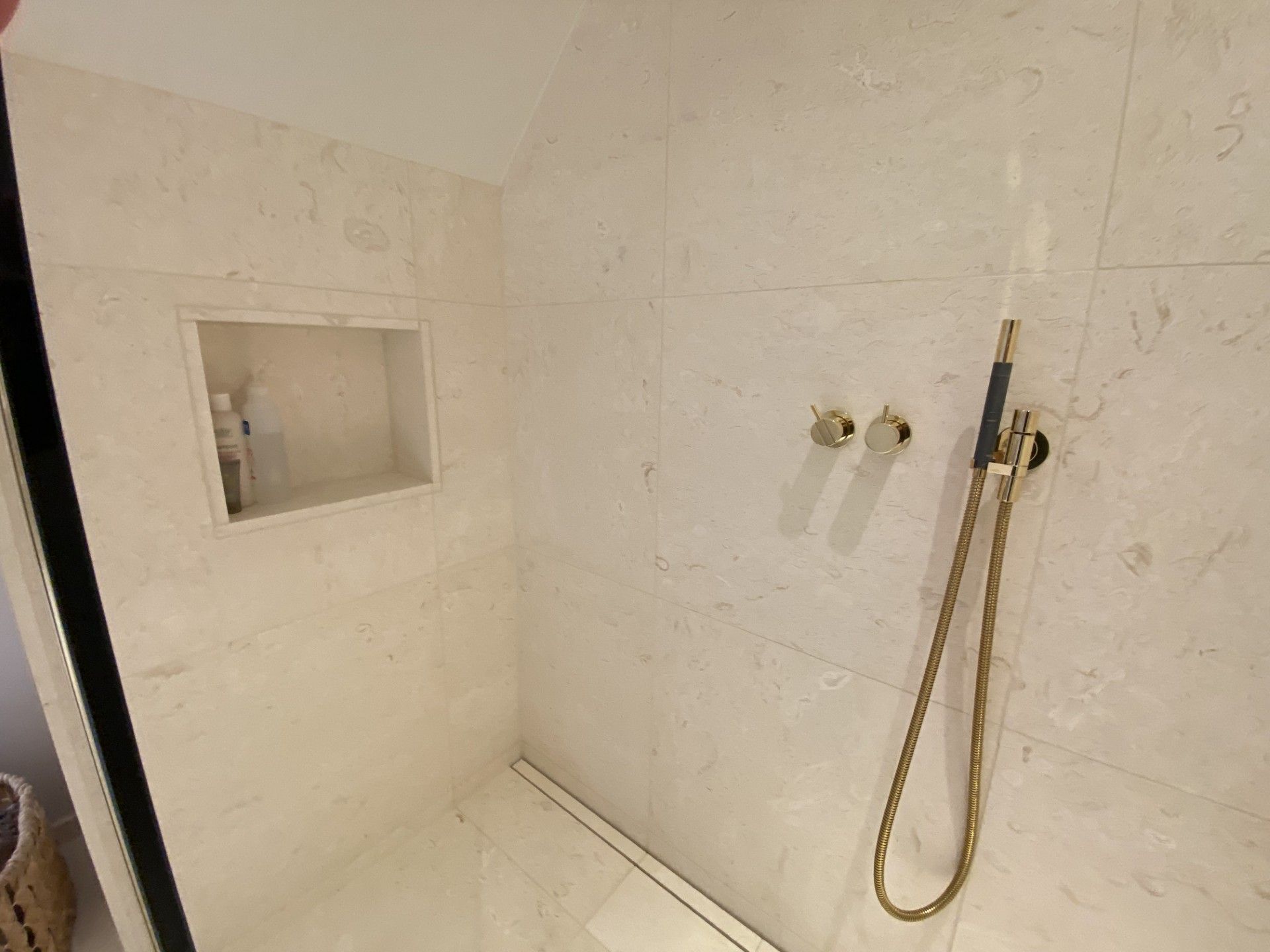 Badeværelsesbruser med marmorlignende fliser, en indbygget hylde og gyldne brusearmaturer.
