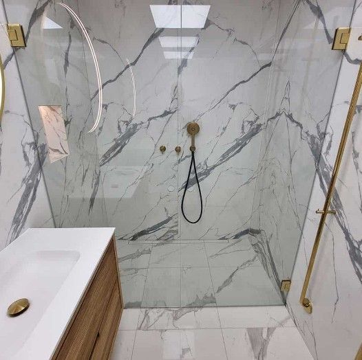 Elegant badeværelse med marmorvægge, bruseniche i glas og guldarmaturer. Træbordplade med hvid vask.