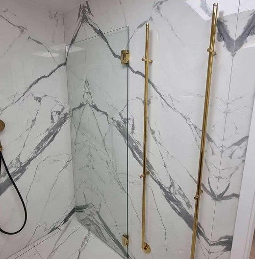 Brusekabine med marmorfliser, guldarmaturer og glaslåge. Marmoren har grå årer.