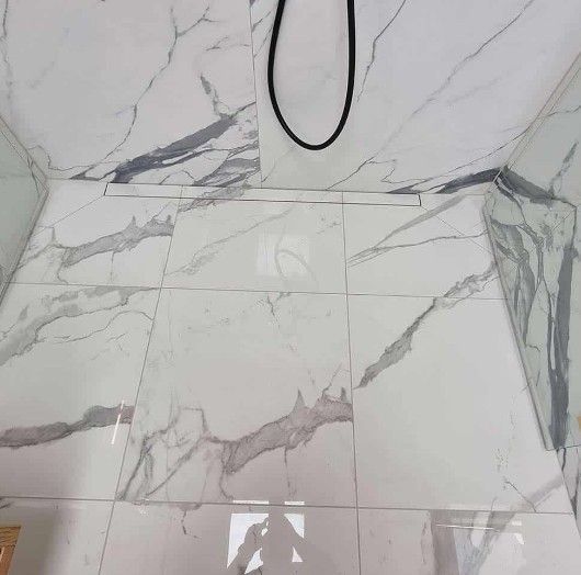 Brusegulv med hvid marmorfliser, lineært afløb og sort bruserslange.