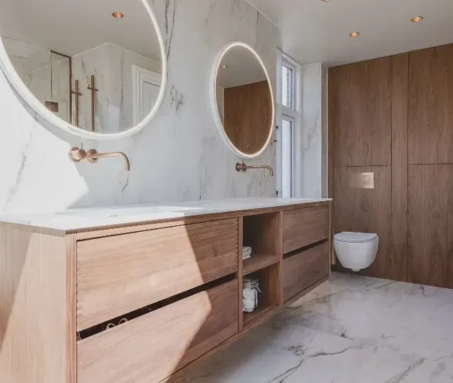 Moderne badeværelse med dobbelt håndvask, marmordetaljer og træskabe.