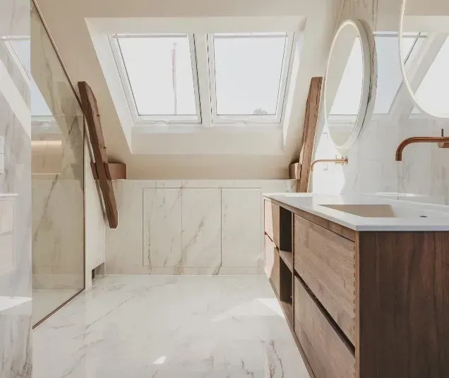 Moderne badeværelse med marmorvægge og træbordplade under ovenlysvindue.