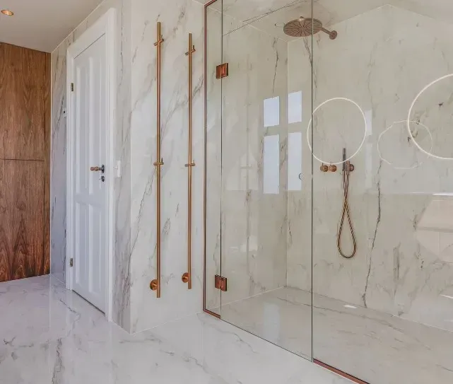 Luksuriøst badeværelse med marmorvægge og kobberarmaturer, inklusive bruser og dørhåndtag.