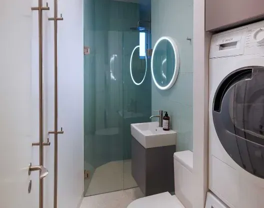 Lille moderne badeværelse med glasbruser, svævende vask og vaskemaskine/tørretumbler.