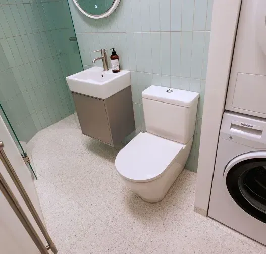 Badeværelse med vægmonteret vask, toilet og vaskemaskine. Blå vægge, hvidt gulv.