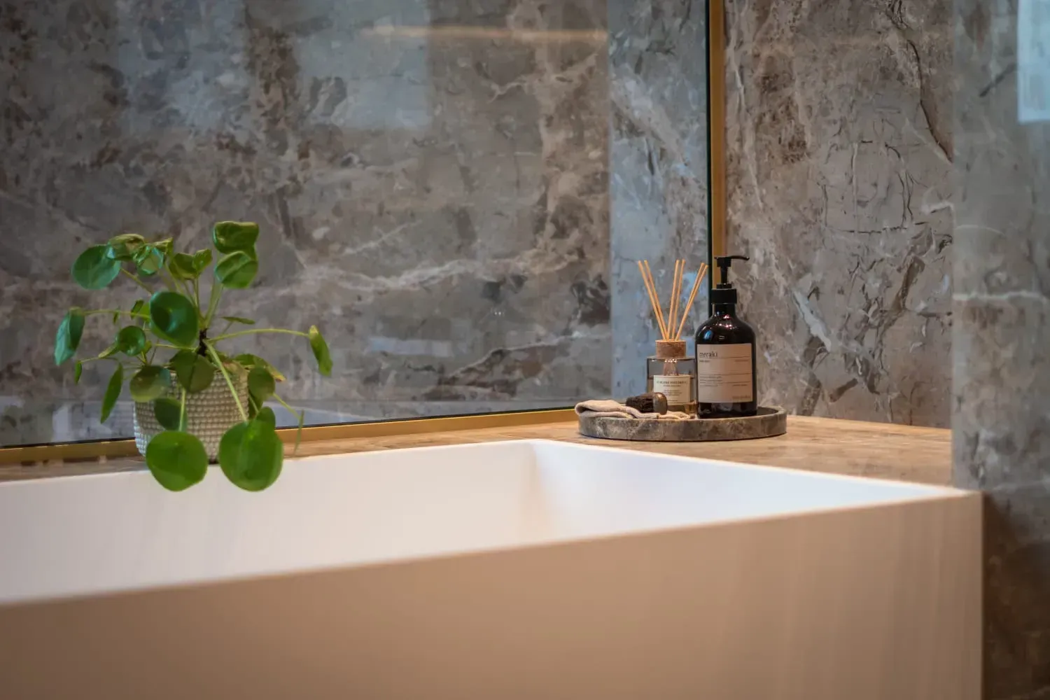 Hvidt badekar med marmorvæg, plante og toiletartikler.