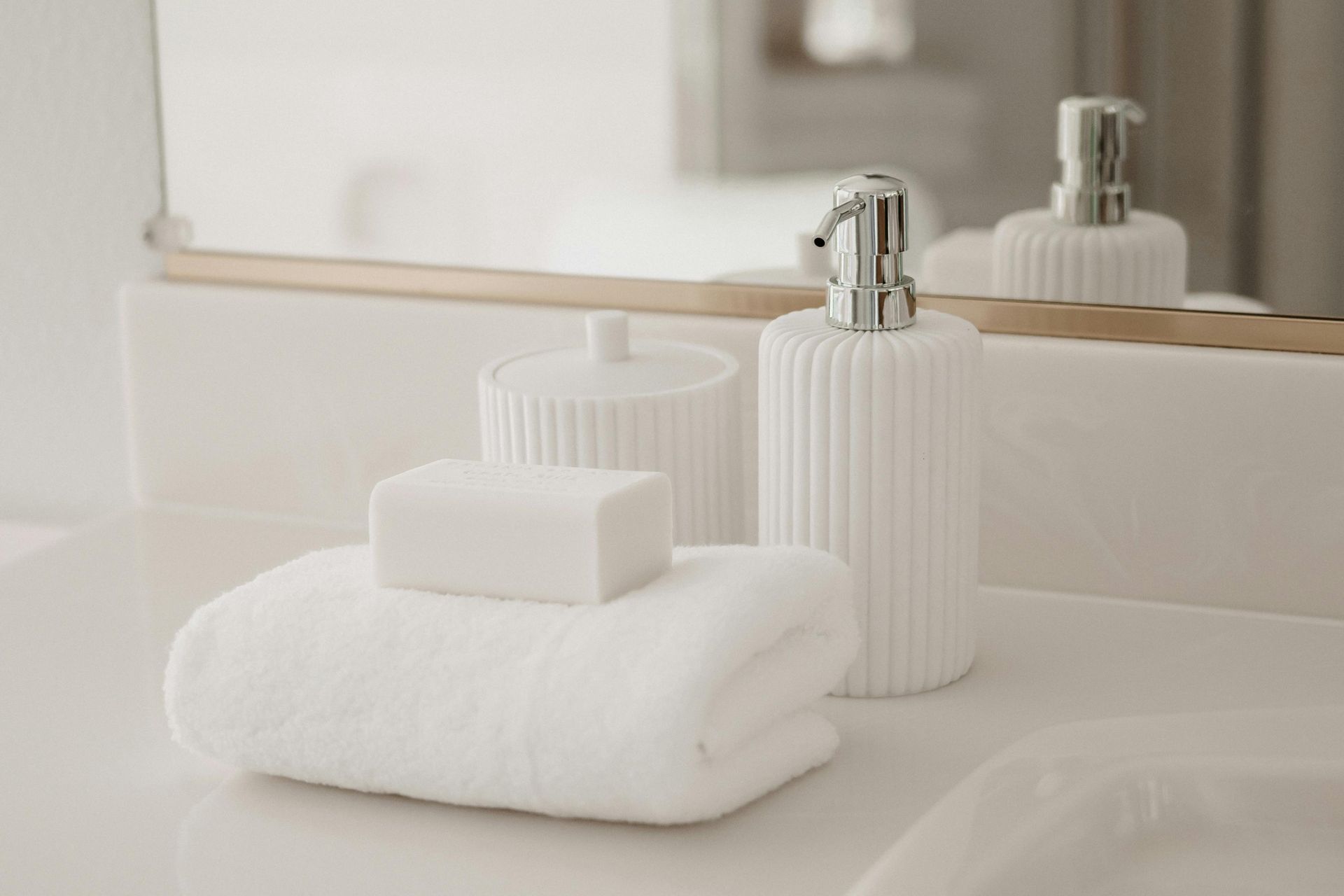 Hvid badeværelsesbordplade med et foldet håndklæde, en sæbestykke, en sæbedispenser og en beholder foran et spejl.