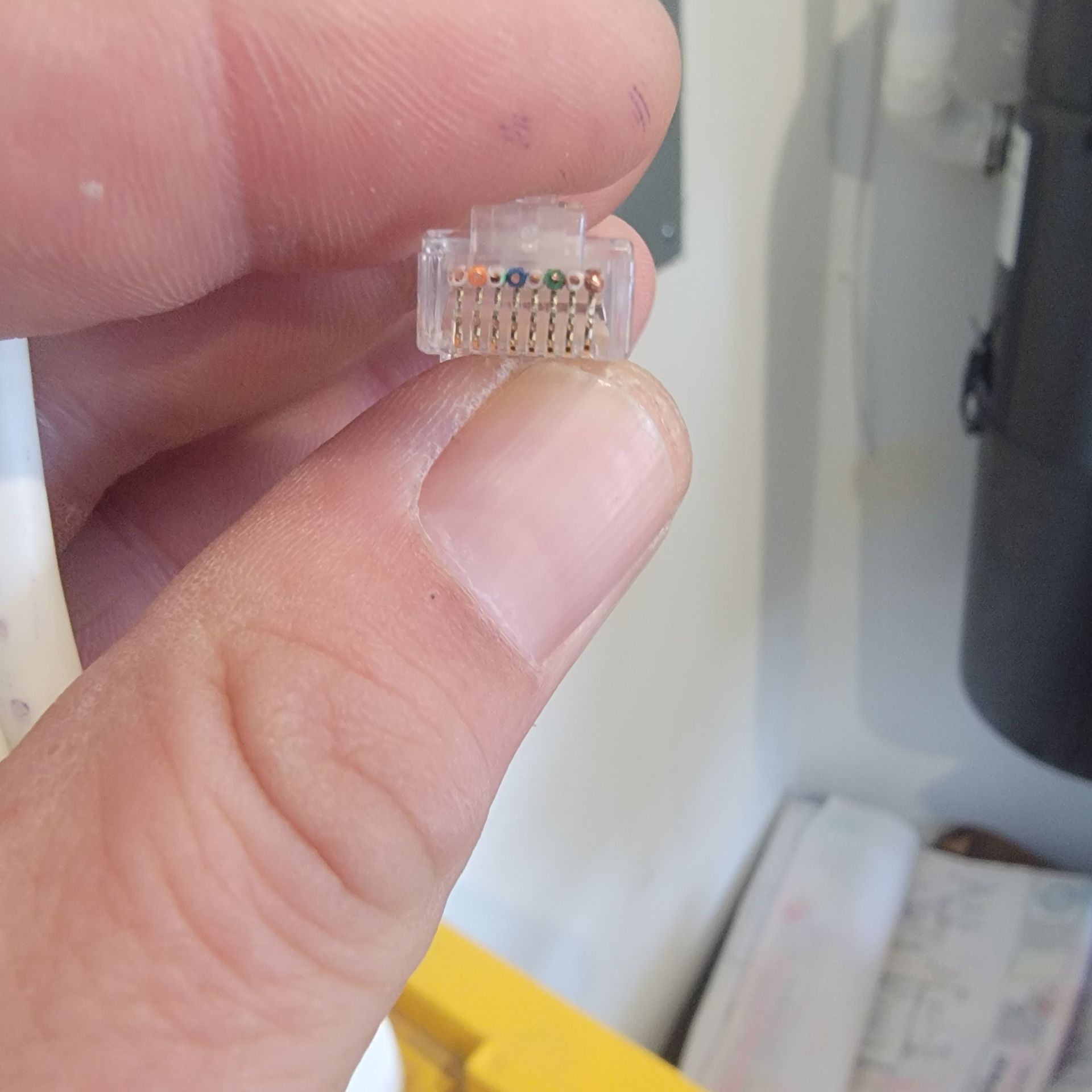 Hand holding an RJ45 Ethernet connector; wires visible.