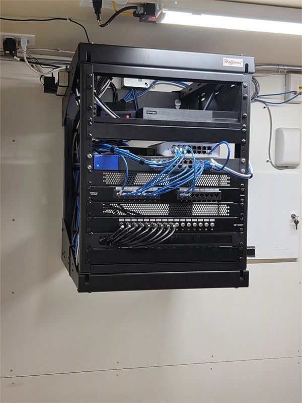 Black network rack mounted on a white wall, filled with network devices and blue cables.