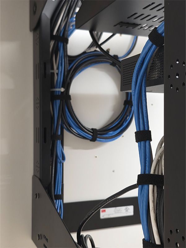 Black network rack with neatly organized blue and black cables secured by Velcro straps.