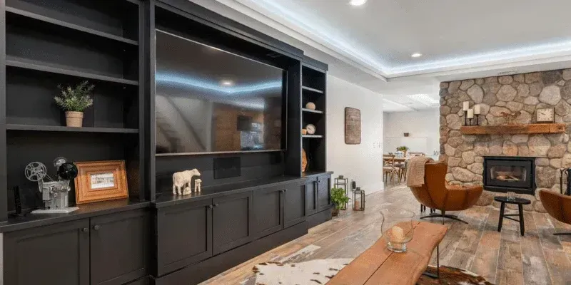 Living room with a stone fireplace, large TV unit, wood floor, and leather chairs.