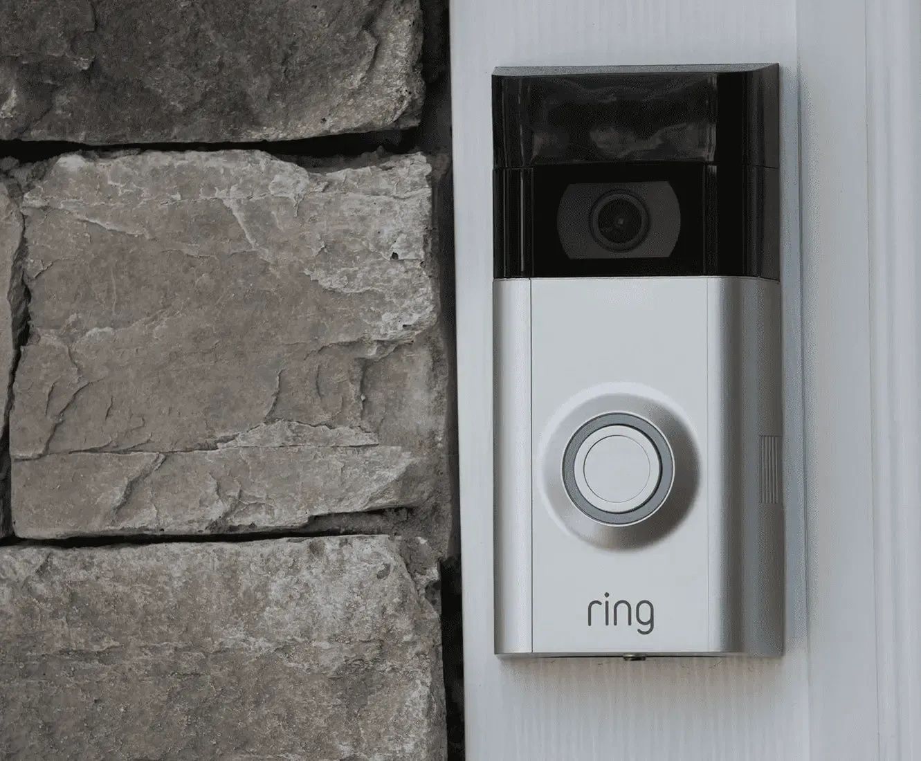 Ring video doorbell mounted beside a white front door on a stone exterior wall