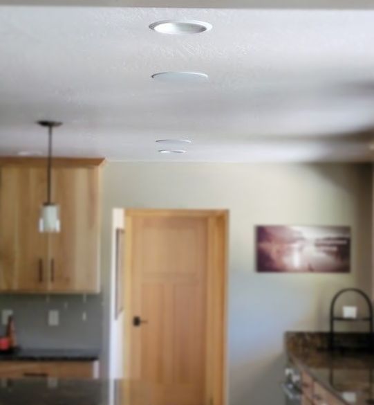 Recessed ceiling lights in a kitchen with wooden cabinets, door, and countertop.