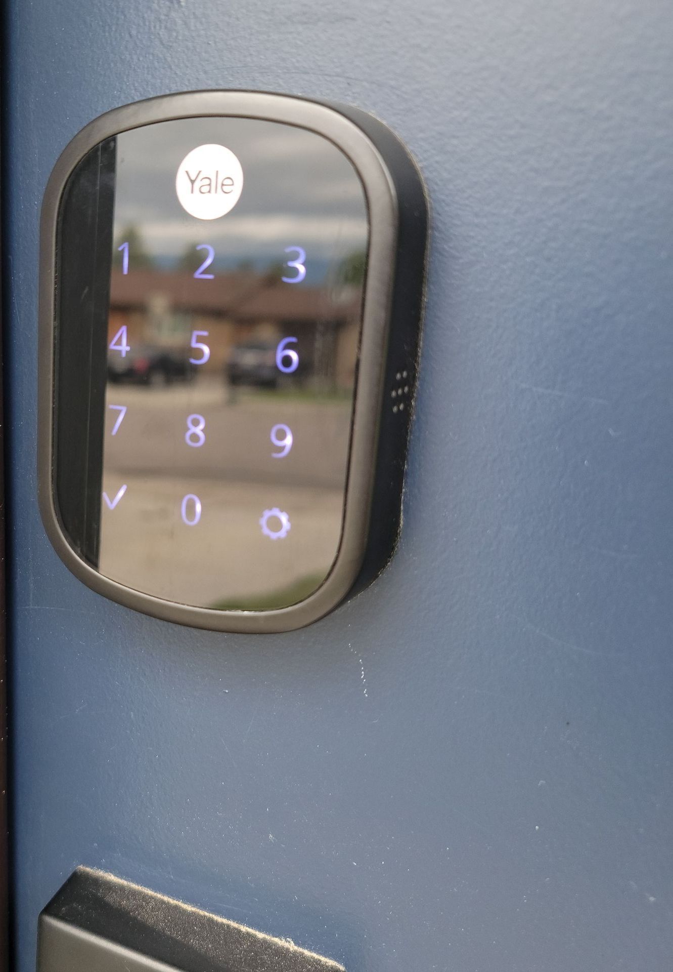 Black Yale keypad lock on a blue door, with numbers lit up.