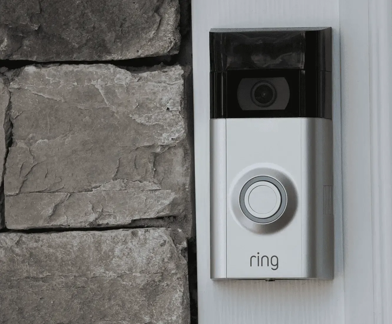 Silver Ring doorbell mounted on a stone wall, next to a white door frame.