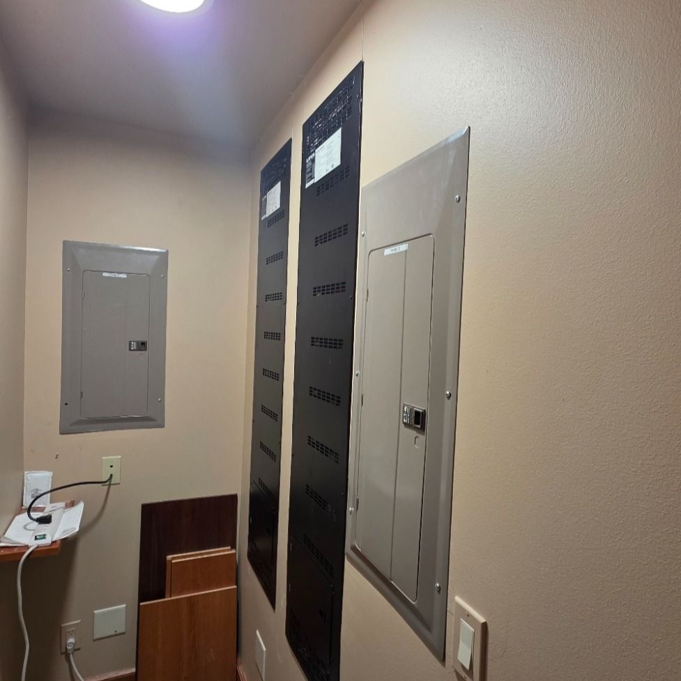 Electrical panel room with several metal panels and dark protective coverings on a beige wall.