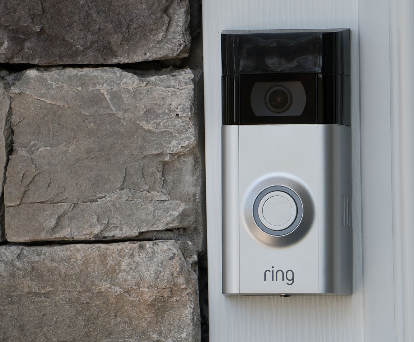 Silver Ring doorbell mounted on a stone wall, next to a white door frame.