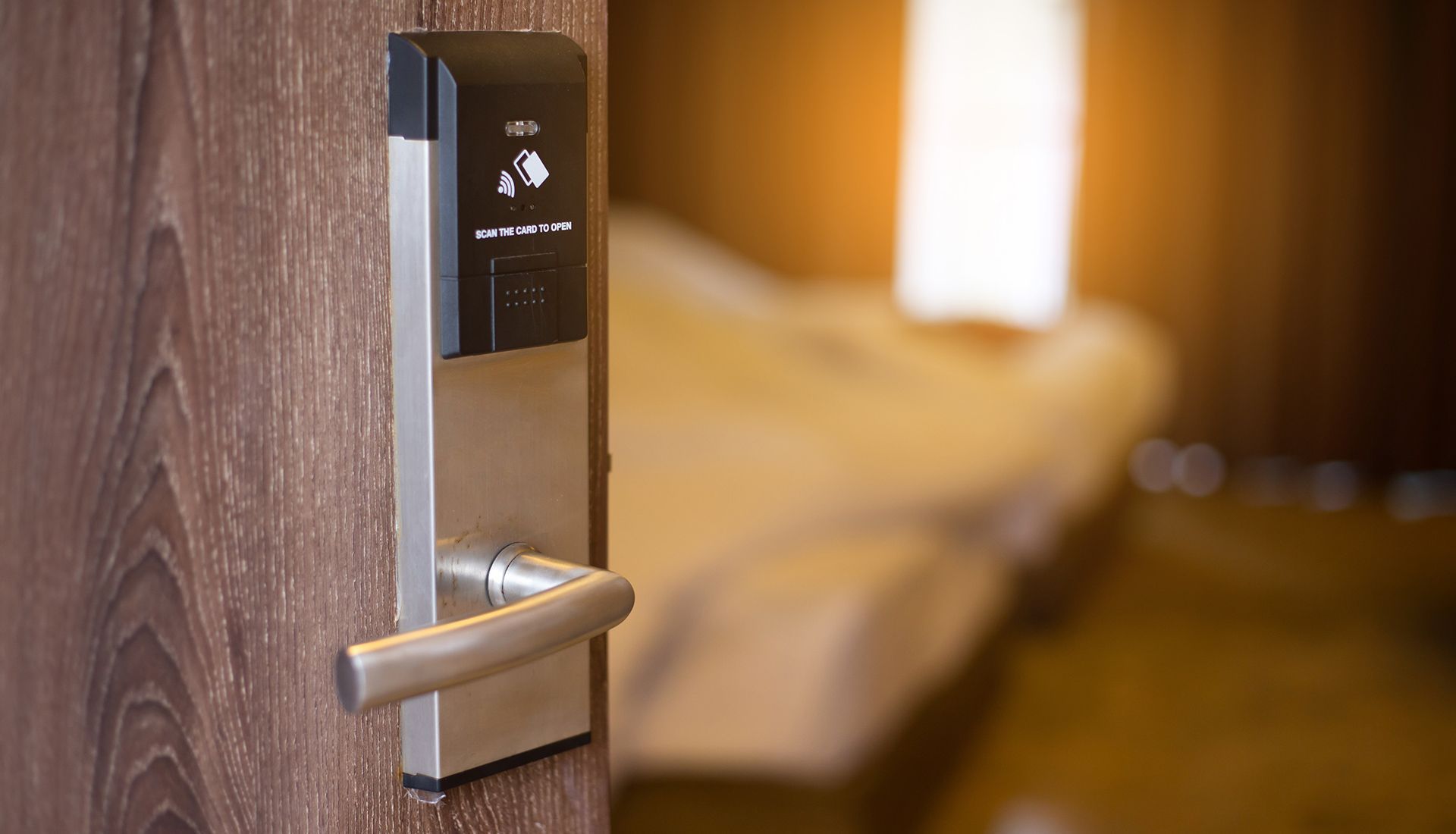 Hotel room door ajar, showing a bed in the blurred background. Door has a card reader.