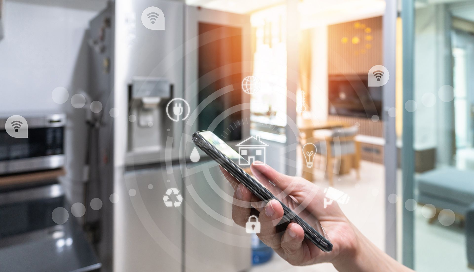 A hand holding a phone, interacting with smart home icons in front of a refrigerator in a kitchen.
