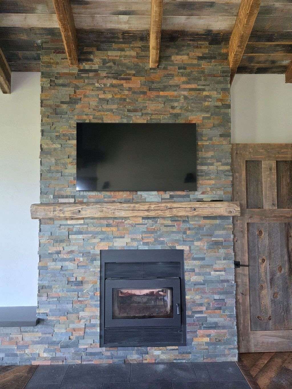 TV mounted above slate stone fireplace with rustic wood beam ceiling — Smart Home Solutions MT
